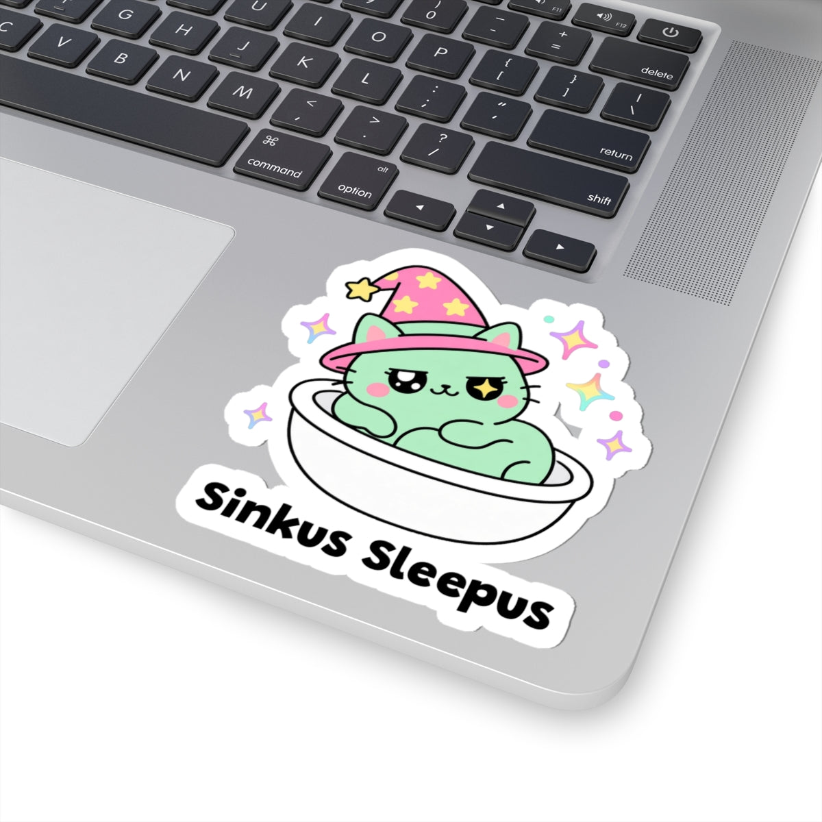 Sinkus Sleepus wizard cat sticker stuck on a silver laptop next to the keyboard
