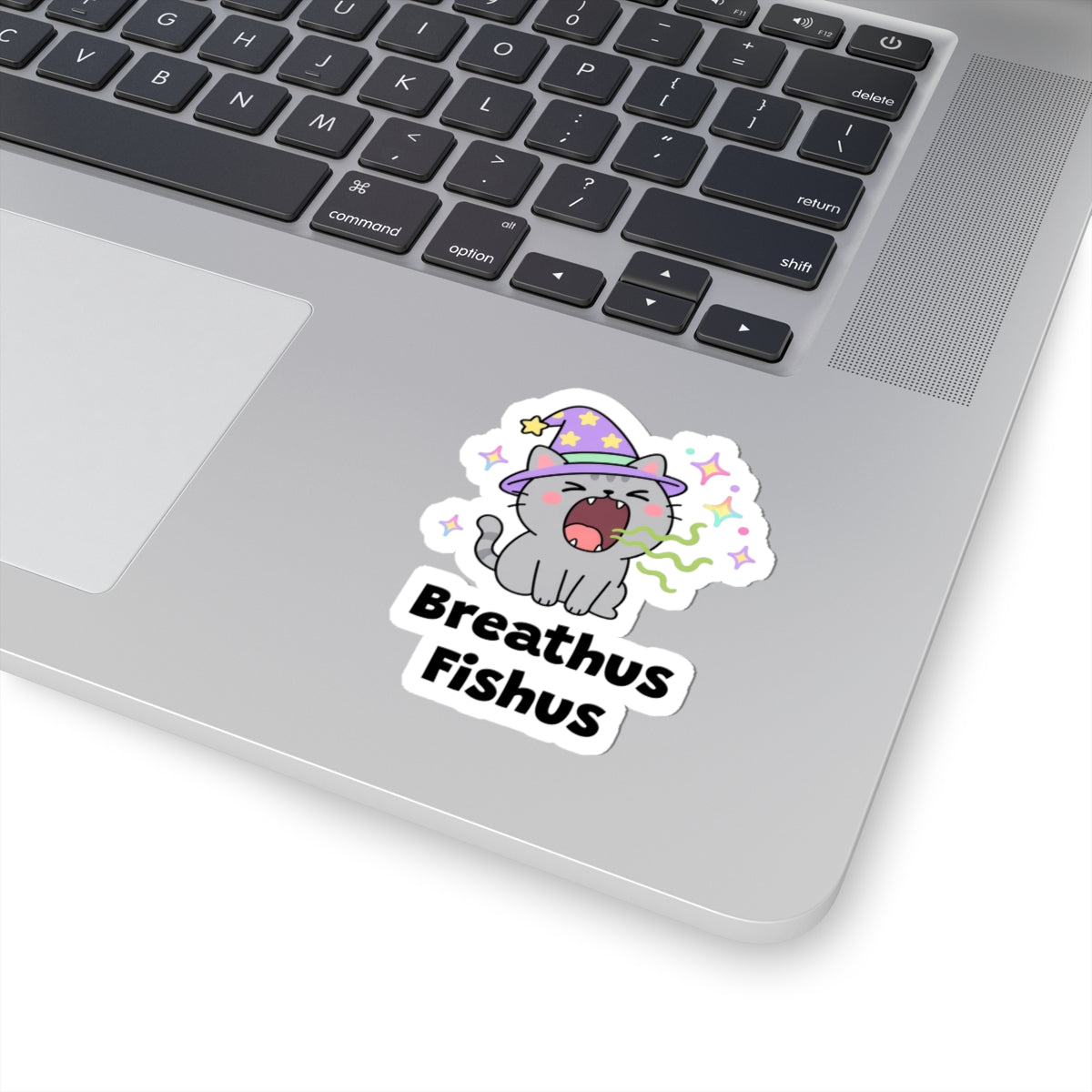 Breathus Fishus wizard cat sticker stuck on a silver laptop next to the keyboard