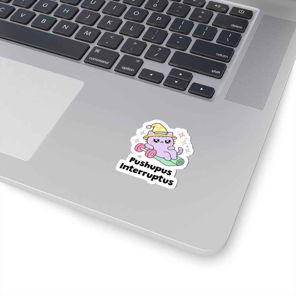 Pushupus Interruptus wizard cat sticker stuck on a silver laptop next to the keyboard