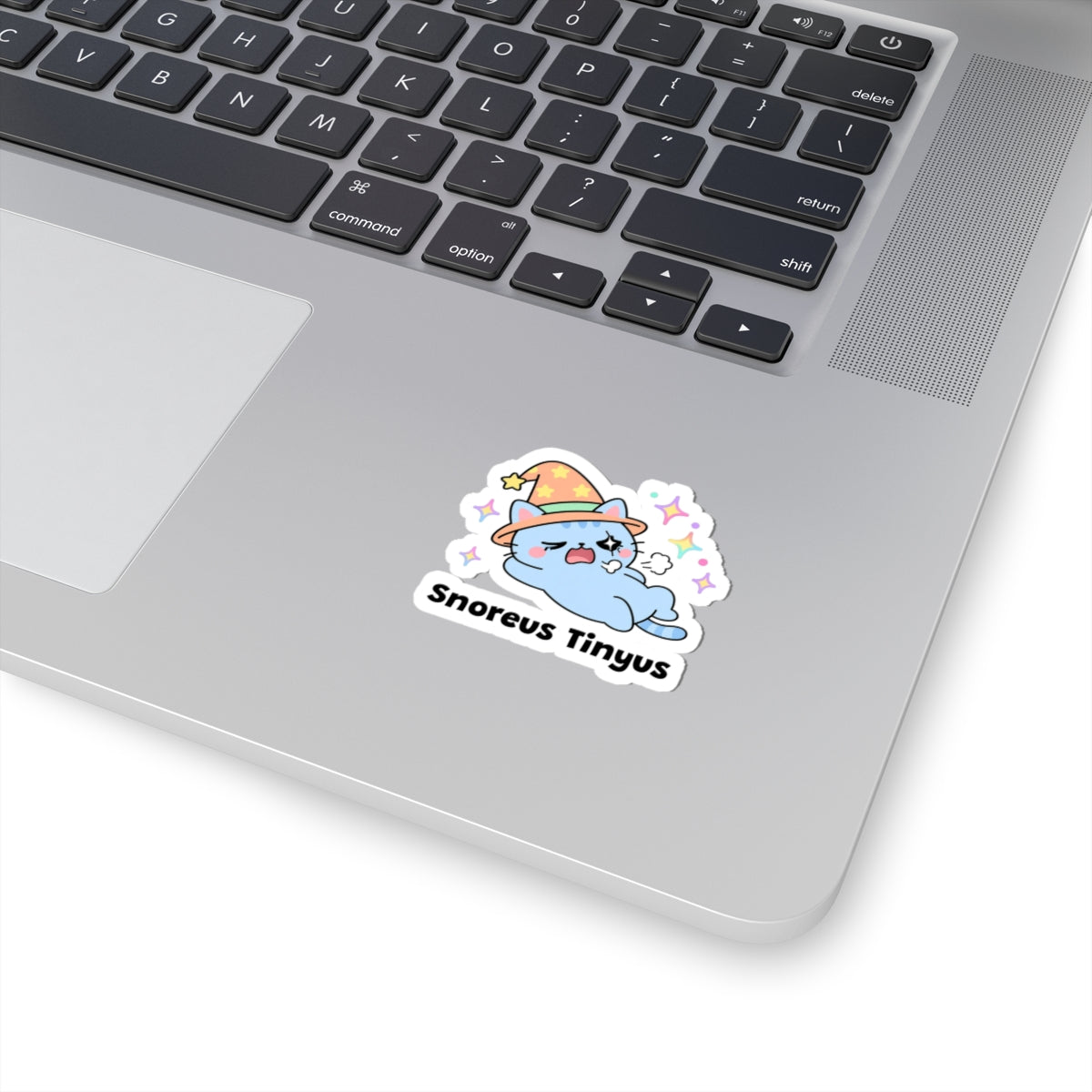 Snoreus Tinyus wizard cat sticker stuck on a silver laptop next to the keyboard