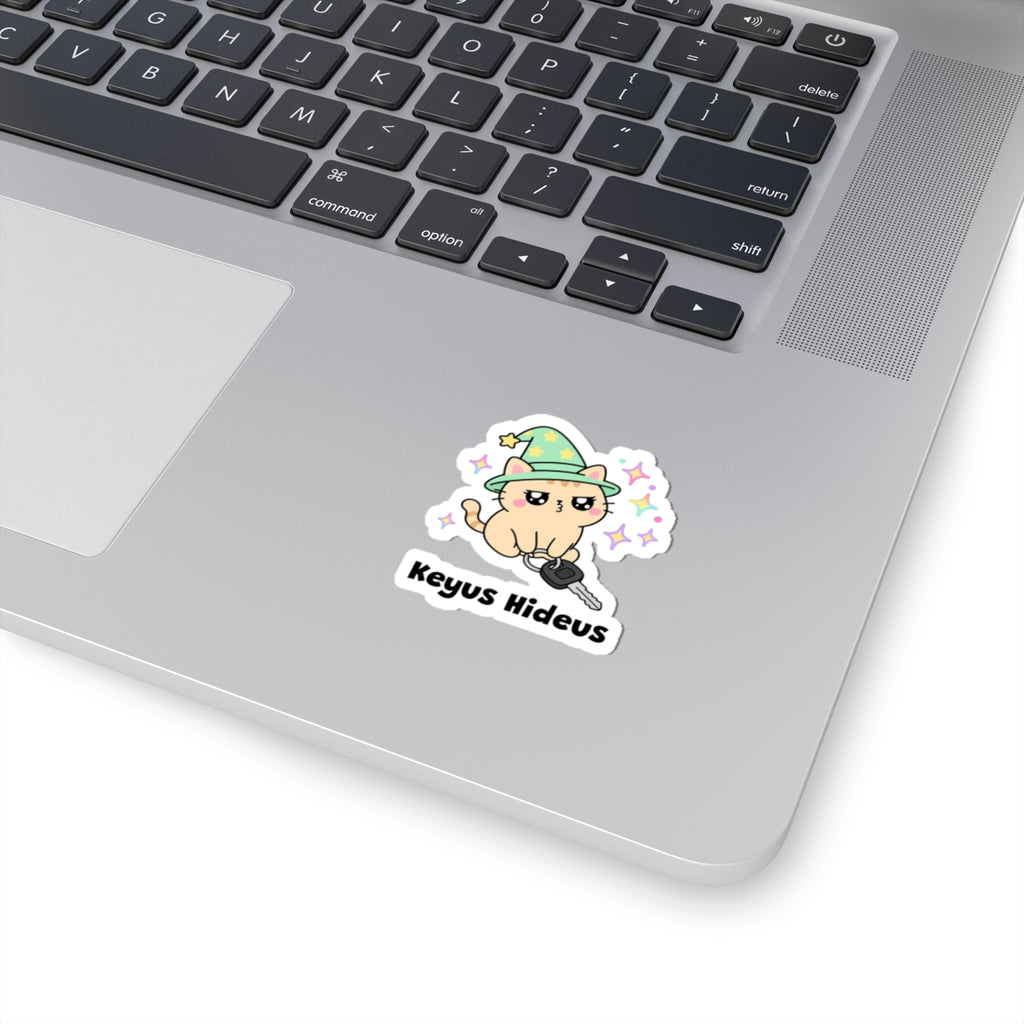 Keyus Hideus wizard cat sticker stuck on a silver laptop next to the keyboard