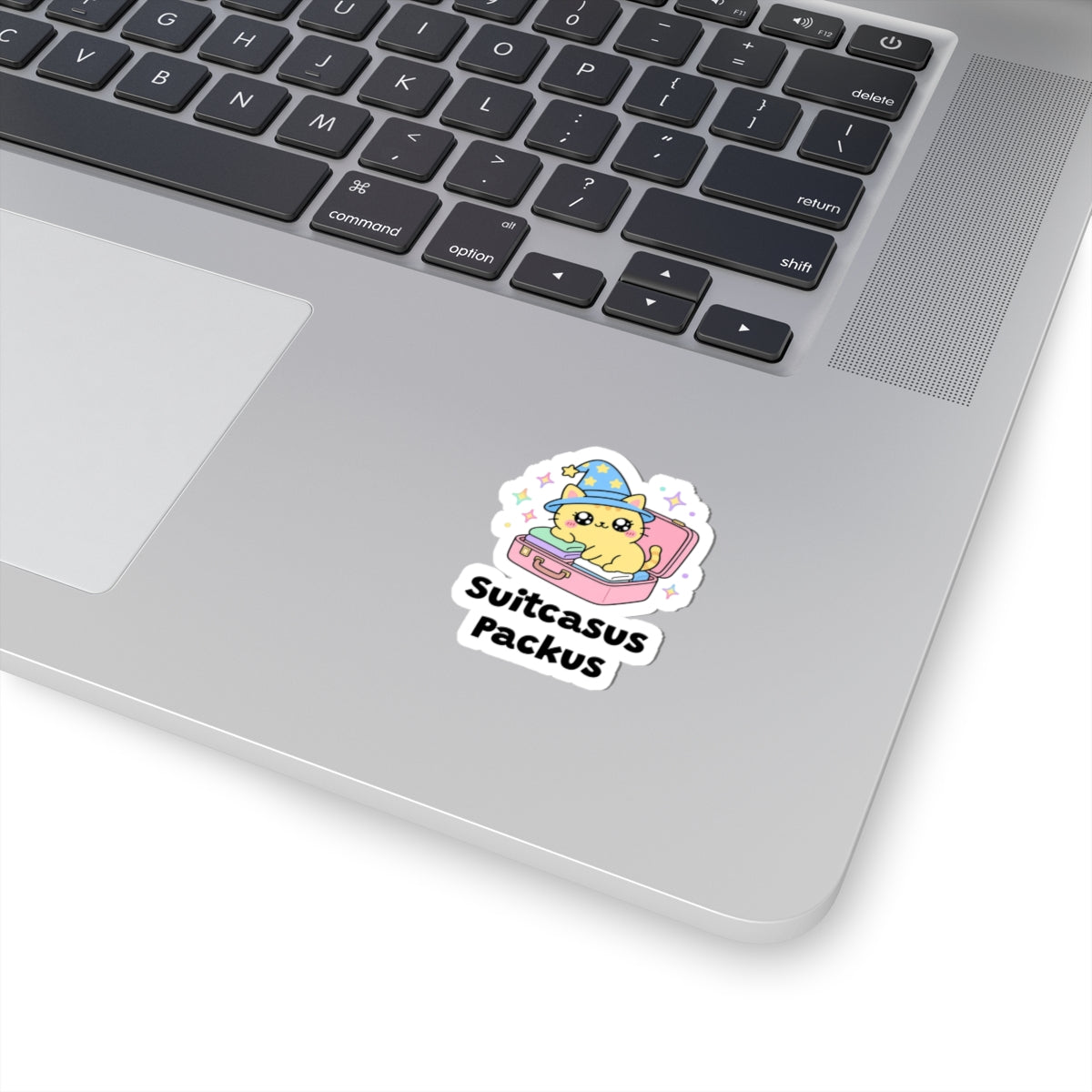 Suitcasus Packus wizard cat sticker stuck on a silver laptop next to the keyboard