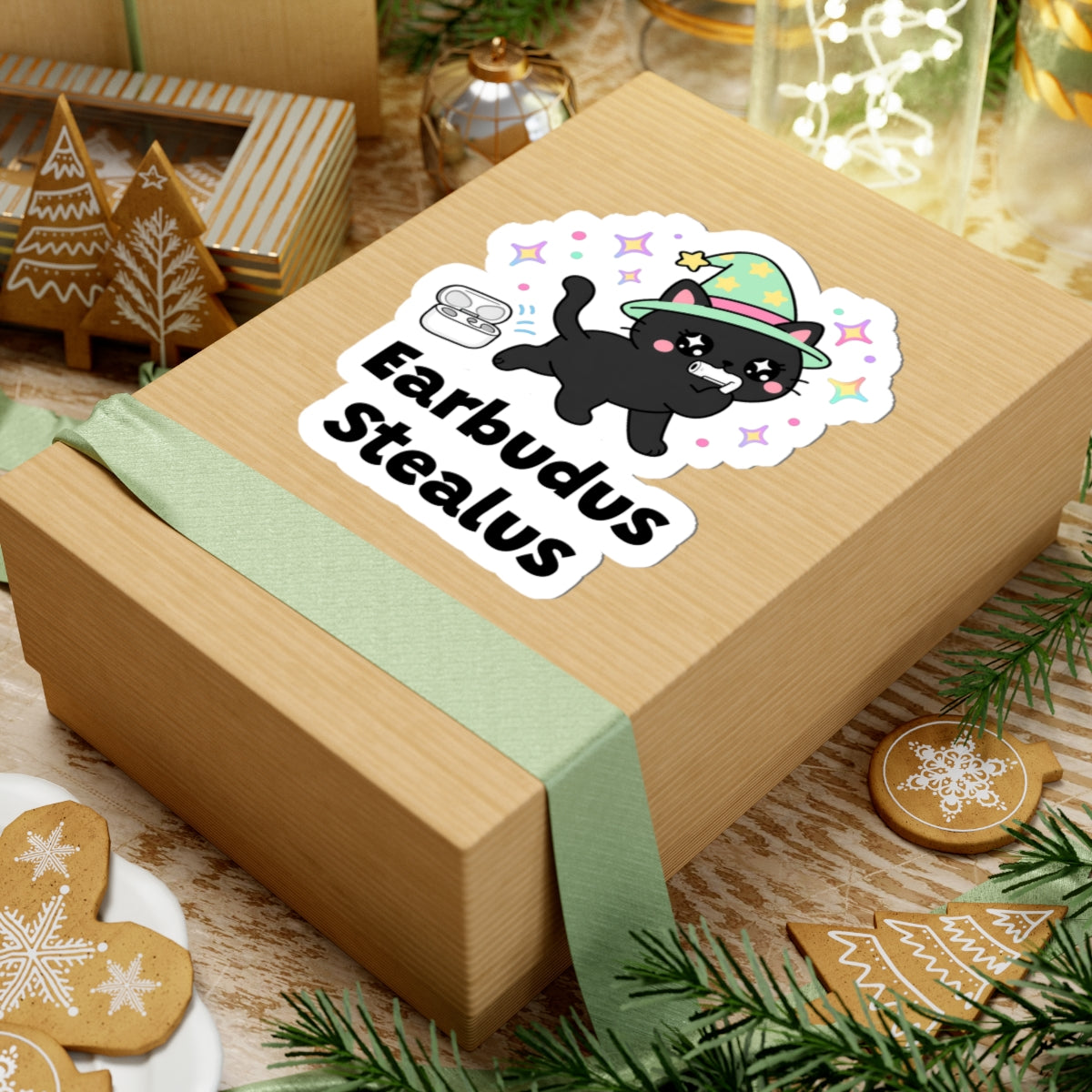 Earbudus Stealus wizard cat sticker on a kraft gift box with a green ribbon and holiday cookies